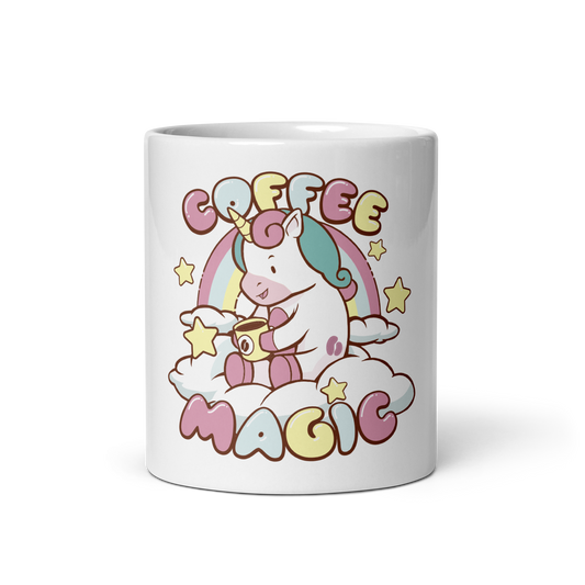 A white ceramic mug featuring a colorful cartoon graphic of a unicorn sitting on clouds and holding a coffee cup, with the words 'COFFEE MAGIC' in pastel bubble letters and small yellow stars.